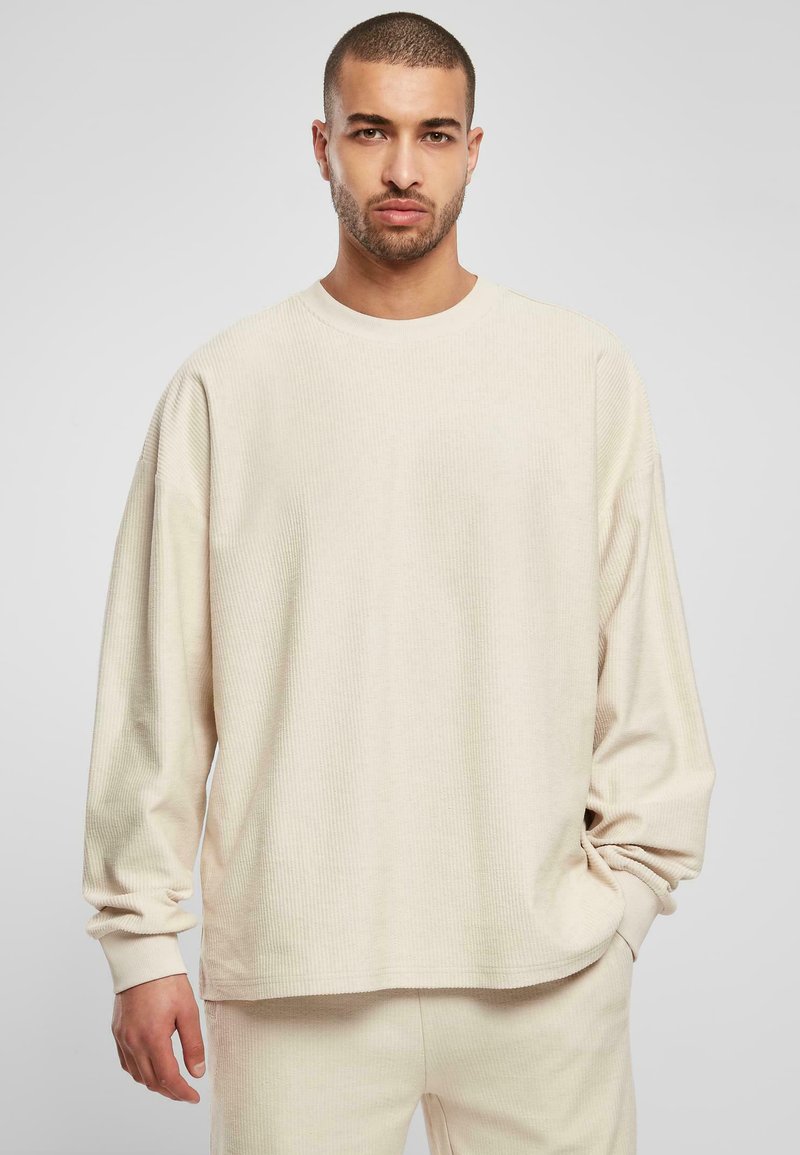 Lichtbeige lange mouwen ribben shirt met een ronde halslijn, losse pasvorm en omgeslagen mouwen. Zachte textuur, minimalistisch ontwerp.
