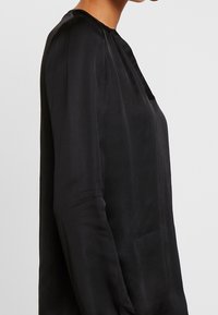 Blusa nera realizzata in tessuto liscio, con scollatura rotonda, maniche lunghe e vestibilità comoda, caratterizzata da dettagli di cucitura minimi.