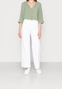 Blusa verde chiaro a scollo a V e con bottoni; pantaloni bianchi a vita alta e a gamba larga; abbinati a sneakers bianche.