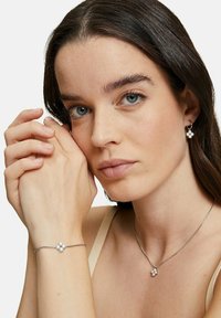 Gioielleria in argento con un design floreale e tre perline bianche. Include orecchini, bracciale e collana coordinati. Finitura liscia e lucida.