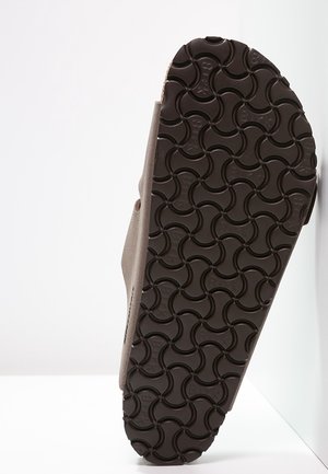 Sole of a beige sandal with dark brown rubber outsole featuring curved, interlocking tread patterns for grip.