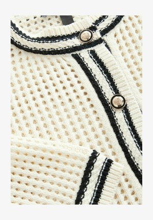Sweter w kolorze kremowym z dzianiny, z teksturowanym wzorem siatki, z czarnymi wykończeniami i guzikami do zapięcia. Wyraźne paski na brzegach.
