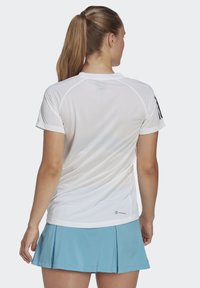 Balta drėgmę sugerianti sportinė marškinė su tekstūruotu orui pralaidžiu audiniu, trumpomis rankovėmis ir juodomis juostelėmis ant pečių. Dėvimi su šviesiai mėlyna sijonu.