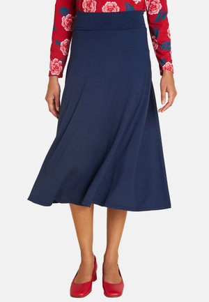 Navyblaue Midirock aus weichem Stoff, mit breitem Bund und fließender Silhouette. Kombiniert mit roten geschlossenen Absätzen.