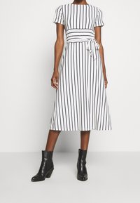 Svart- och vitrandig midi-klänning med korta ärmar, en figursydd kropp och avtagbart knytbälte. Bärs med svarta ankelskor.