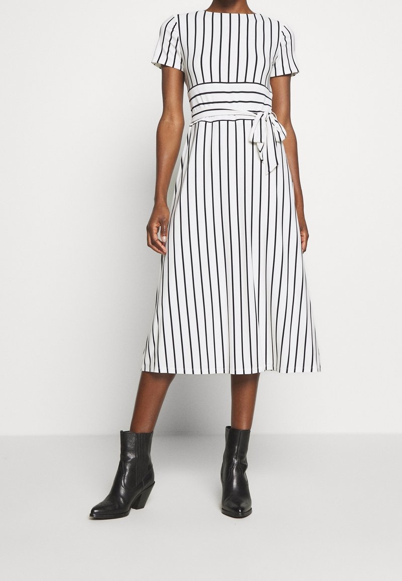 Svart- och vitrandig midi-klänning med korta ärmar, en figursydd kropp och avtagbart knytbälte. Bärs med svarta ankelskor.