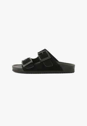 Zwarte slipper met twee verstelbare gespsluitingen en een gestructureerde zool voor grip, weergegeven in een zijaanzicht op een witte achtergrond.