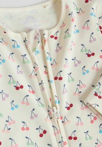 Body pour bébé de couleur crème avec des motifs de cerises multicolores et une fermeture éclair à l'avant munie d'une petite protection en tissu.