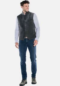 Graue Cordweste mit Stehkragen, Frontknöpfen und zwei Seitentaschen, kombiniert mit einem blau-weiß gestreiften Hemd und Jeans.