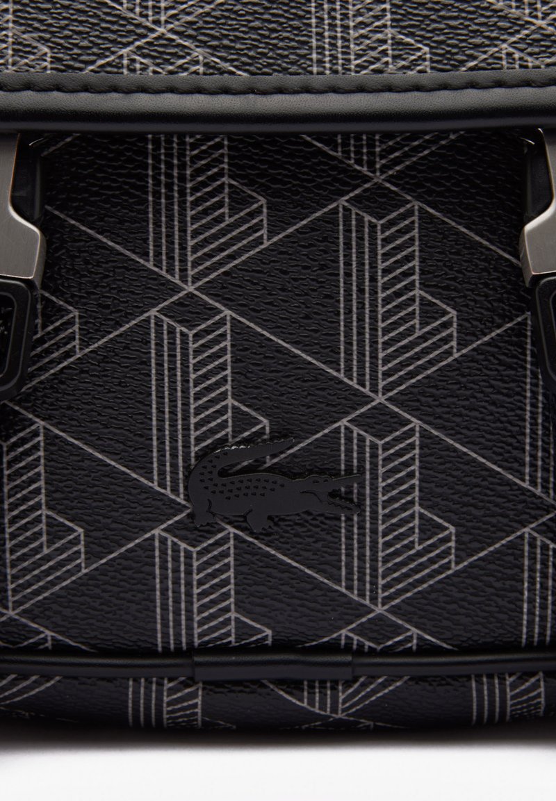 Schwarzes, strukturiertes Material mit einem geometrischen Muster in grauen Linien. Enthält ein kleines schwarzes Krokodil-Logo und metallische Hardware-Details.