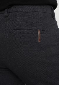 Pantaloni scuri con motivo, caratterizzati da un design aderente, tasca posteriore con etichetta marrone e finitura in tessuto testurizzato.