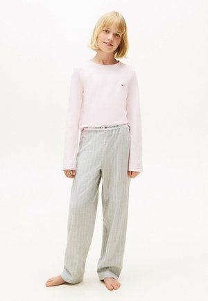 Camisa de manga larga rosa claro con cuello redondeado; pantalones grises a rayas con cinturilla elástica que muestran el logo "TOMMY HILFIGER"; descalzo.