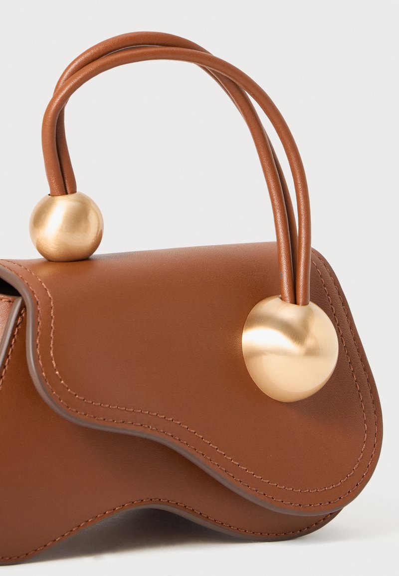 Sac à main en cuir marron avec un design ondulé, doté de doubles poignées fines et de deux accents sphériques dorés. Texture lisse avec des coutures soignées.