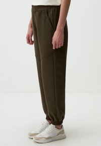 Olijfgroene, taps toelopende sweatpants met een elastische taille en zijzakken, gecombineerd met witte en beige sneakers.