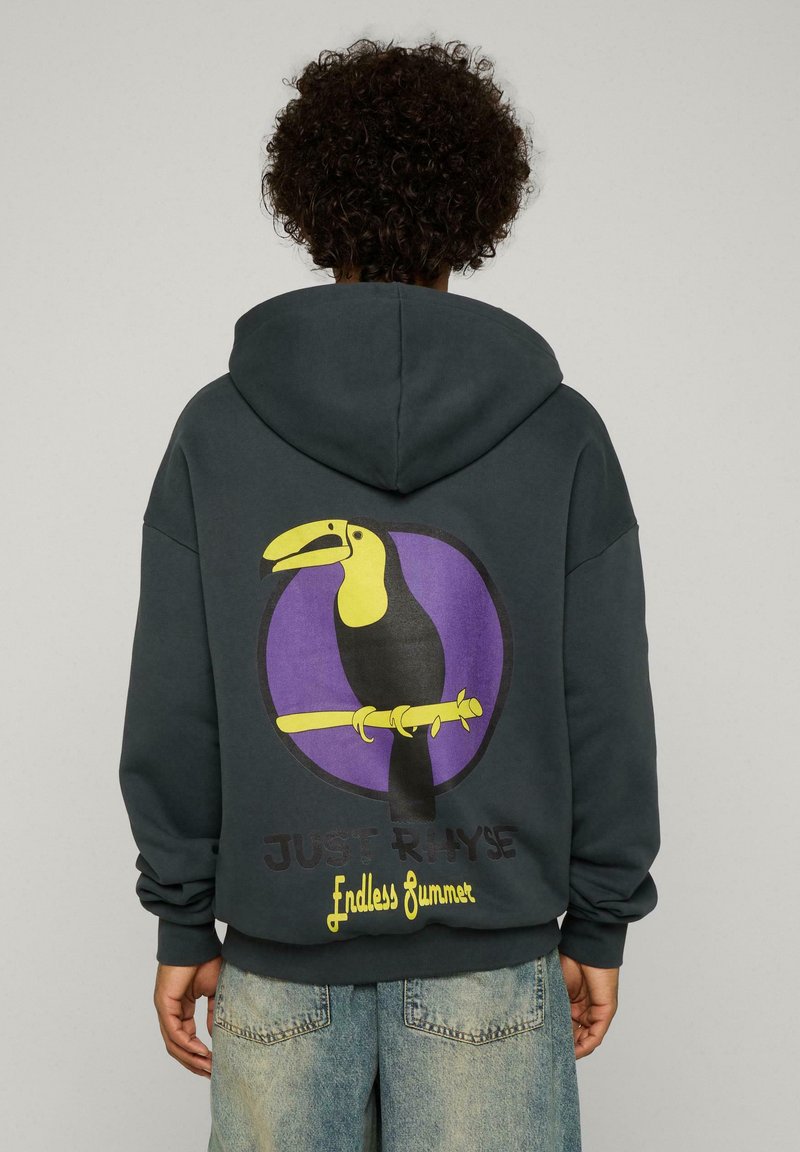 Un hoodie oversized gris foncé avec un graphique de toucan coloré, agrémenté d'accents jaunes, noirs et violets, et du texte "Endless Summer" en bas.