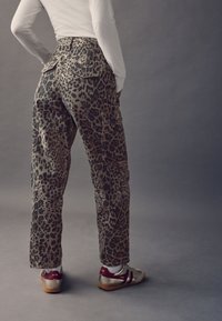 Cargo-Hosen im Leopardenmuster in Beige und Schwarz, mit lockerem Schnitt, Gesäßtaschen, kombiniert mit goldenen Sneakers mit kastanienbraunen Akzenten.