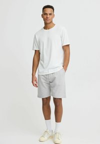 Lys grå bomulds-shorts og en hvid t-shirt med rund hals, der har en afslappet pasform. Bæres med lyse sneakers og hvide sokker.