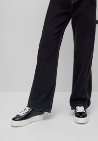Schwarzweitige Jeans mit weißen Nähten, kombiniert mit schwarz-weißen Sneakers mit dicker Sohle und strukturierten Lederakzenten.