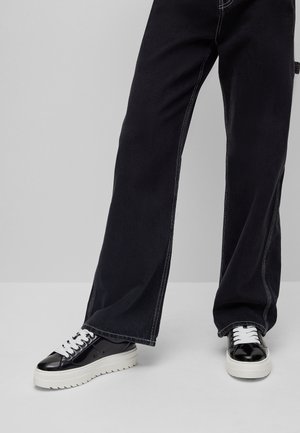 Black wide-leg jeans with white stitching paired with black and white sneakers, featuring a thick sole and textured leather accents.