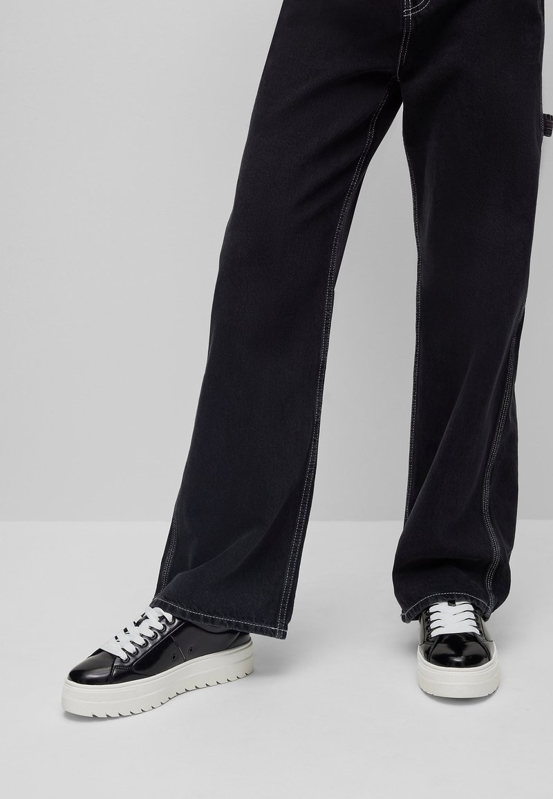 Schwarzweitige Jeans mit weißen Nähten, kombiniert mit schwarz-weißen Sneakers mit dicker Sohle und strukturierten Lederakzenten.
