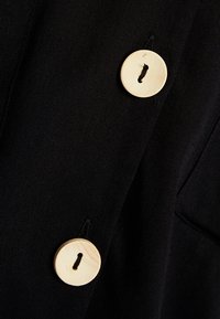 Tissu noir texturé avec deux gros boutons ronds de couleur crème cousus avec du fil noir.