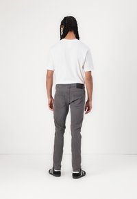 Grå jeans med slim passform, i bomullsmaterial, två bakfickor och en svart tygpatch på midjebandet. Bärs med en enkel vit t-shirt.