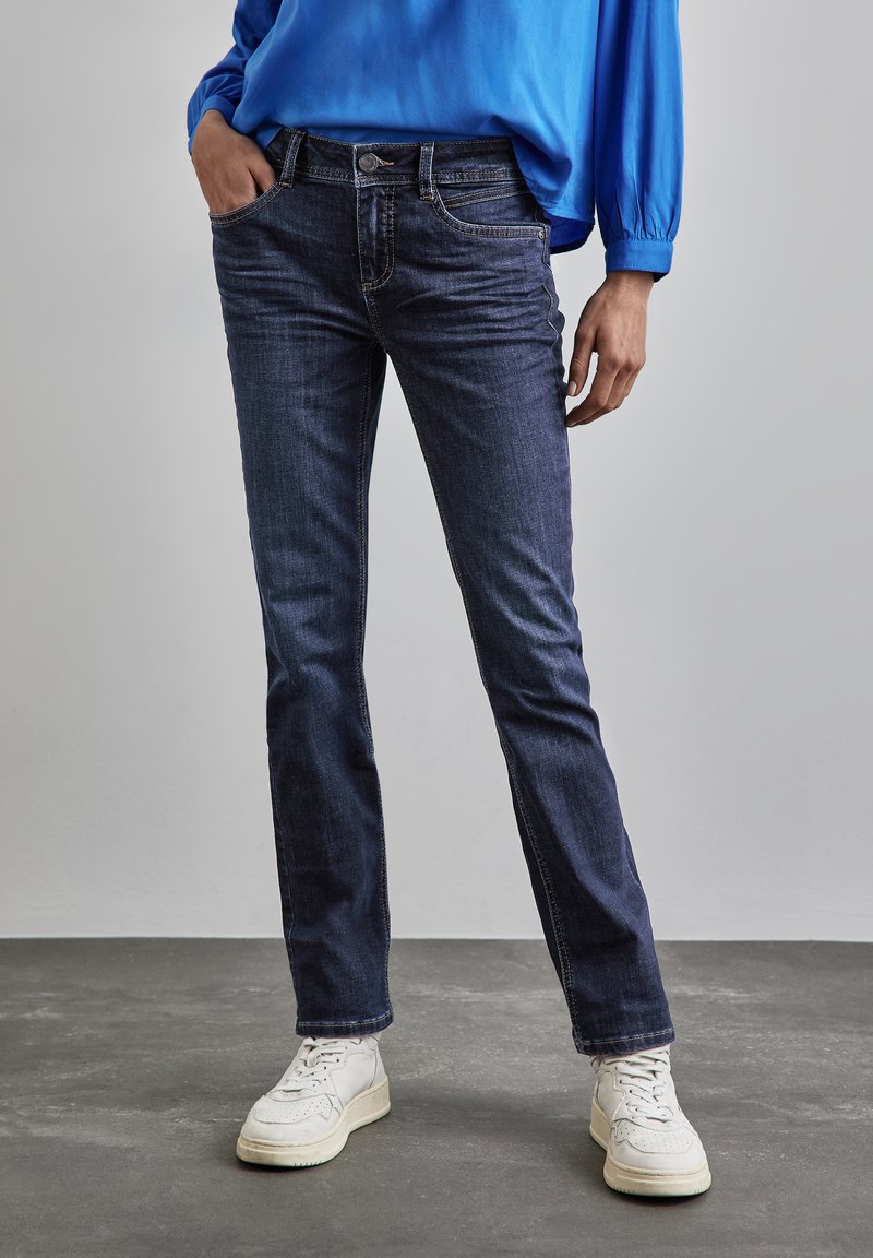 Mörkblå denimjeans med rak passform, femfickorsdesign och synliga sömdetaljer, kompletterat med vita sneakers.
