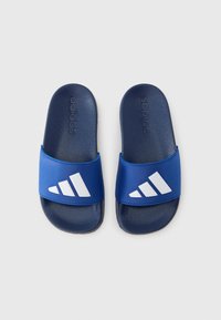 Modré pantofle na klínu s texturovanou tmavě modrou stélkou a hladkým modrým páskem s bílým logem tří pruhů.