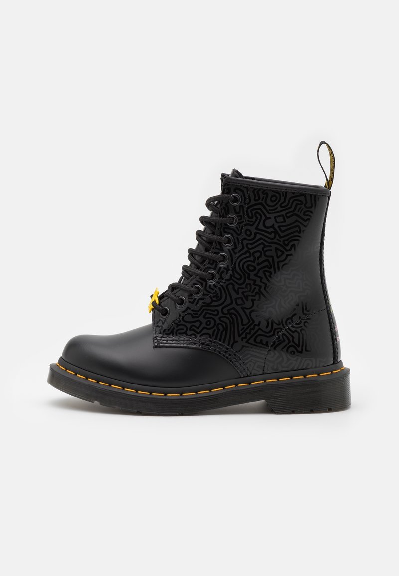 Botas de tobillo negro con cordones, diseño estampado, ojales amarillos y costuras amarillas, con punta redonda y suela de goma resistente.