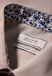 Il colletto della camicia beige presenta una fodera con motivo floreale blu e giallo. Le etichette riportano la scritta "JACK'S" e "COMFORT FIT." Dettagli del tessuto testurizzato ben visibili.