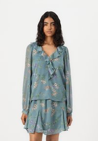 Blouse florale bleu clair avec un col à volants et des manches longues, associée à une jupe plissée assortie. Présente un motif de fleurs délicat.