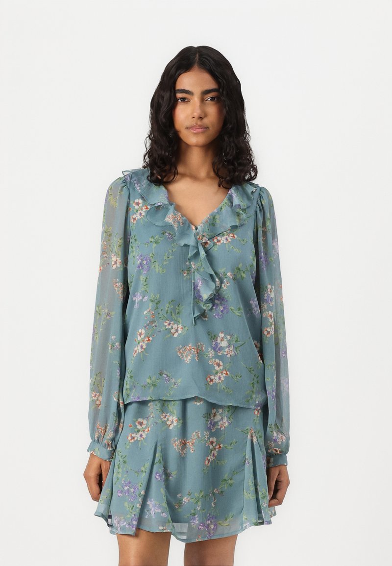 Blouse florale bleu clair avec un col à volants et des manches longues, associée à une jupe plissée assortie. Présente un motif de fleurs délicat.