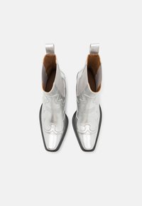 Botas de vaquero plateadas con punta afilada, material de cuero, costuras decorativas y una suela negra. Incluyen tiradores para facilitar el calzado.