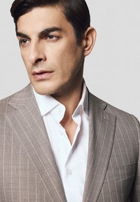 Jasnoszara marynarka w paski o delikatnych prążkach, noszona na białej koszuli, z klapami w kształcie notcha, o gładkiej fakturze i nowoczesnym, dopasowanym kroju.