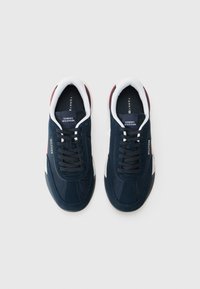 Sneaker blu navy con materiali scamosciati e sintetici, dettagli bianchi, punta rotonda, lacci piatti e dettagli rossi sul tallone.