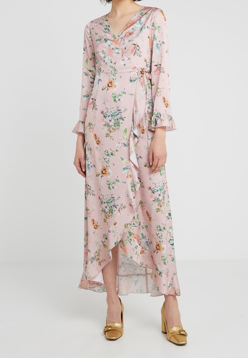 Robe longue fleurie en tissu rose pâle, avec manches longues, col en V et détails volantés. La robe présente un design portefeuille et des motifs floraux colorés.