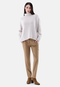 Hellrosa gestrickter Pullover mit einem hohen Kragen, kombiniert mit beigefarbenen, taillierten Hosen und braunen, schmalen Stiefeletten mit Absatz. Einfacher, lässiger Schnitt und Textur.