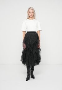 Juodas tiulio ilgas sijonas su sluoksniuotais volanais ir taškinio rašto, derinamas su paprasta balta trumpomis rankovėmis palaidine ir juodais aukštais batais iki kelių.