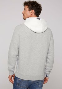 Felpa grigia in cotone con cappuccio bianco, polsini e orlo a coste. Presenta un'etichetta con logo sul retro e dettagli laterali blu.