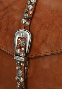 Braune Lederhandtasche mit einer silbernen Schnalle und dekorativen metalischen Akzenten entlang des Riemens, darunter verschiedene Formen und Texturen.