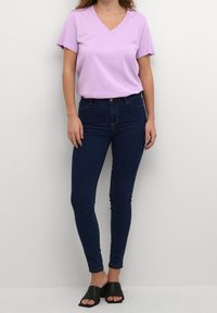 Lyse lilla V-hals t-shirt med korte ærmer, parret med mørkeblå skinny jeans. Sorte slidse sandaler fuldender outfittet.