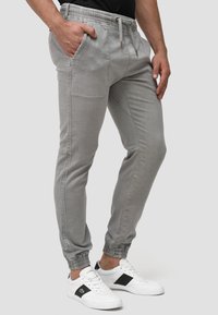 Pantalones jogger gris claro de mezcla de algodón. Cintura elástica con cordón, bolsillos laterales y tobillos ajustados. Textura suave.