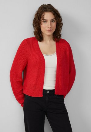 Rode gebreide cardigan met een textuurstof, open voorkant en ribbel-details. Gedragen over een witte top, gestyled met zwarte jeans.