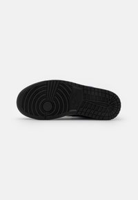 Suela negra de zapatilla Nike con patrones de tracción circulares y en cuadrícula sobre un fondo blanco.