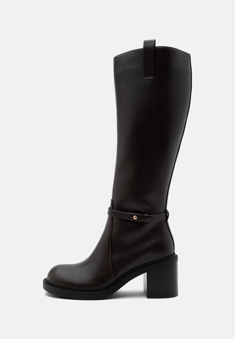Botte en cuir noire mi-mollet avec talon bloc, bride décorative avec petite clou doré au-dessus de la cheville et languette de tirage en haut.