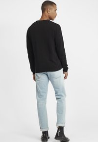 Black long-sleeve sweater, ribbed cuffs and hem, paired with light blue jeans and black ankle boots, viewed from the back.