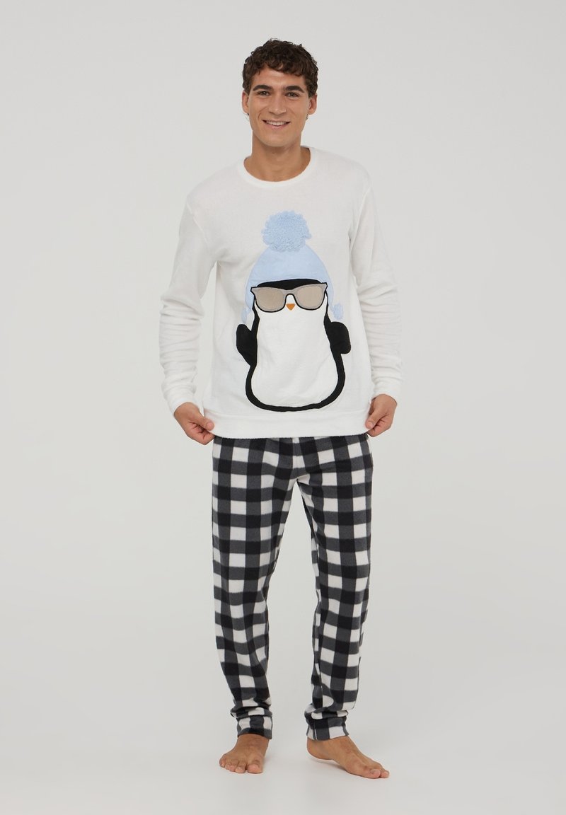 Maglione bianco a maniche lunghe con design di un pinguino che indossa occhiali e un cappello blu. Pantaloni da pigiama in pile a scacchi bianchi e neri.