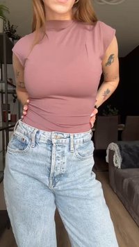 Top aderente color malva con collo alto abbinato a jeans a vita alta in denim chiaro. Tessuto liscio senza motivi o decorazioni visibili.