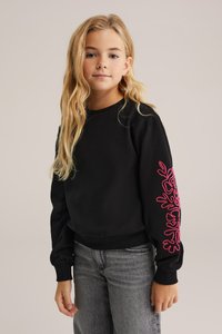 Melns džemperis ar garām piedurknēm, kuram kreisajā rokā ir rozā izšūta ziedu dizaina kompozīcija. Ribotie piedurkņu gali un apakšmala nodrošina ciešu piegulšanu.