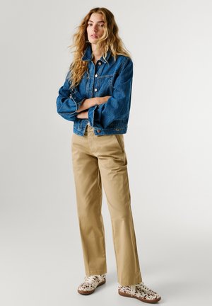 Chaqueta vaquera azul oscuro con cierre de botones, pantalones caqui con bolsillos laterales y zapatillas blancas con un patrón sutil.